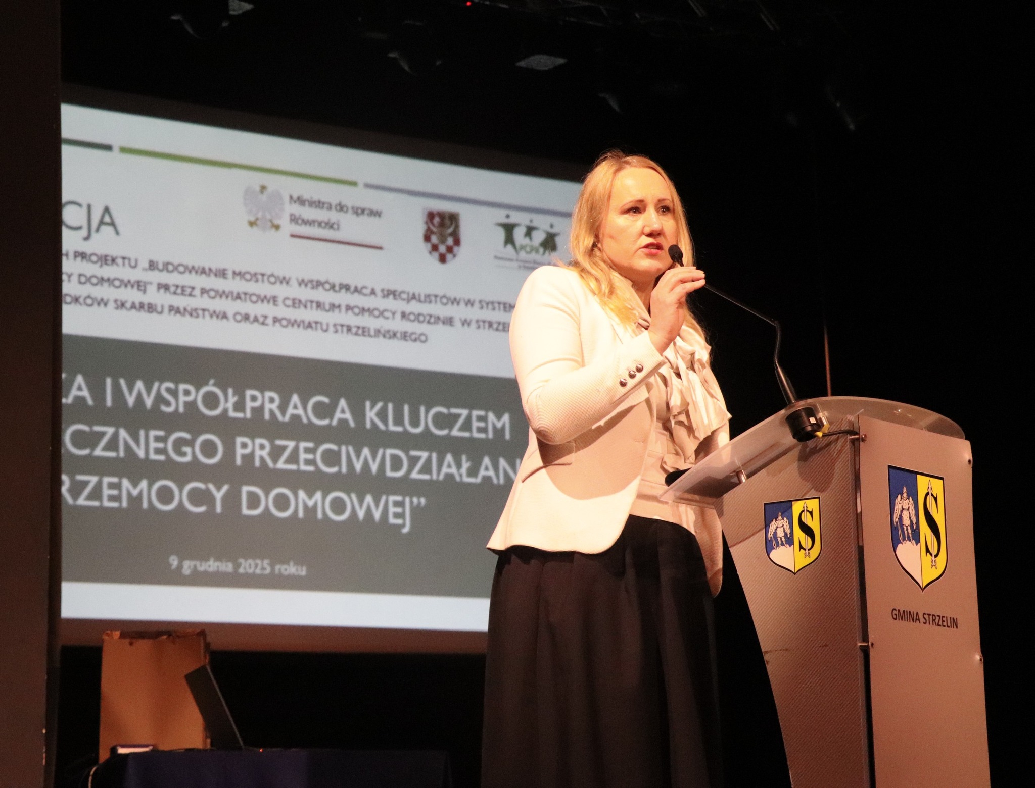 Kobieta wygłasza przemówienie przy mównicy, skupiając uwagę słuchaczy.