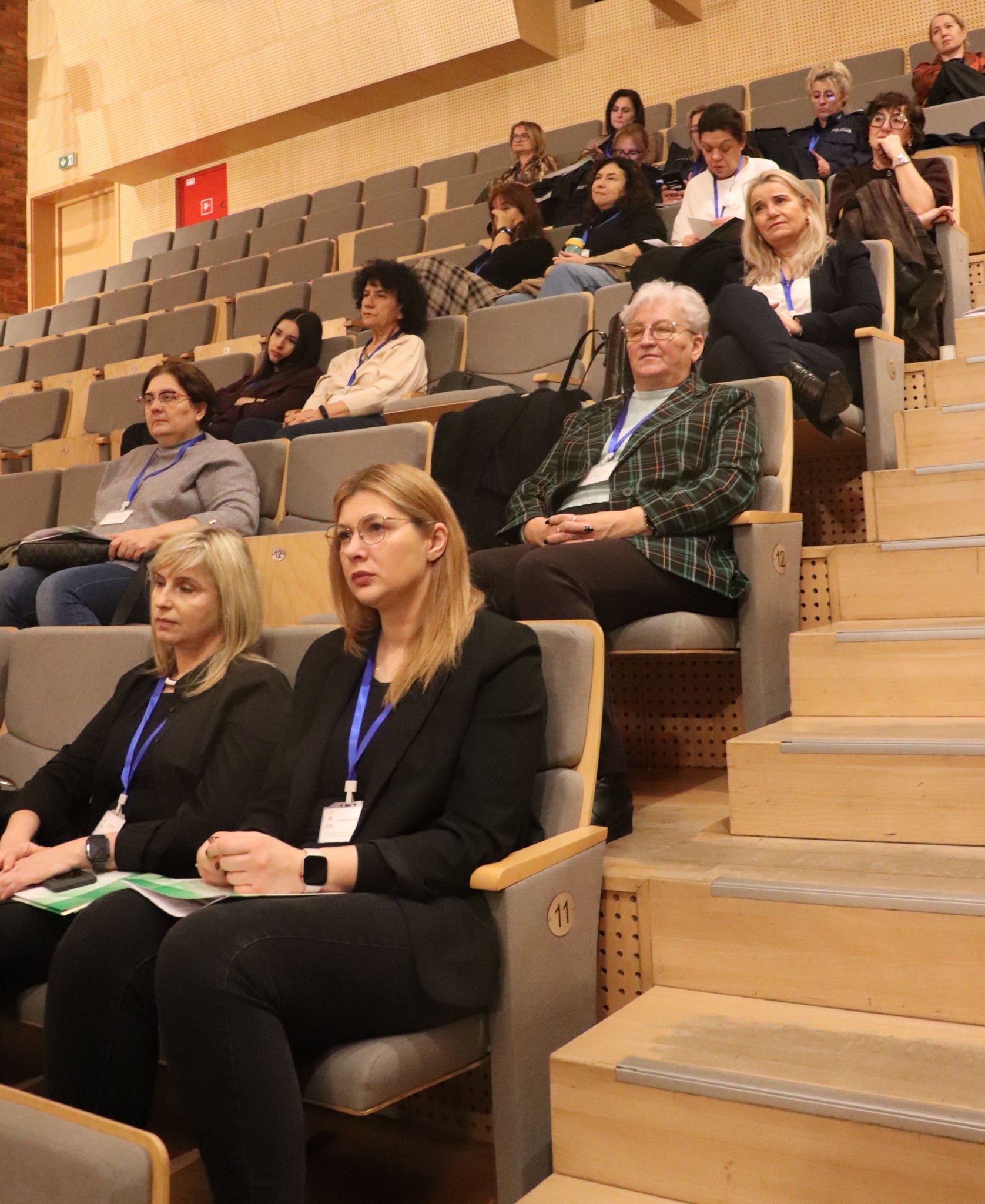 Grupa ludzi siedząca w dużym audytorium, zwrócona w stronę sceny.