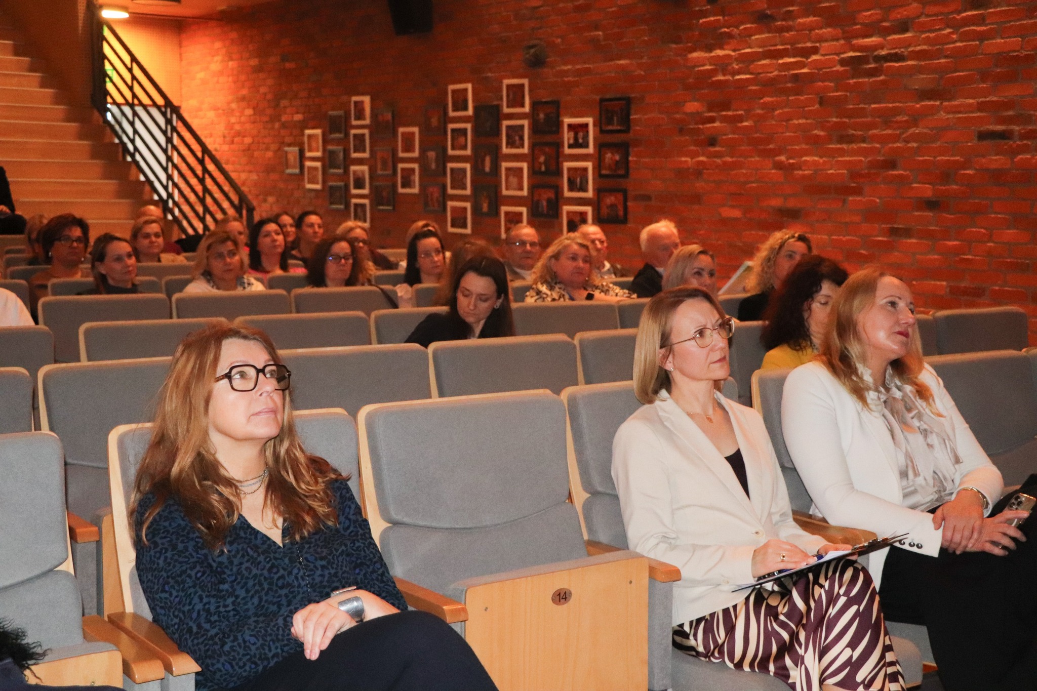 Grupa kobiet siedzących na krzesłach w sali wykładowej, uważnie słuchających prelekcji.