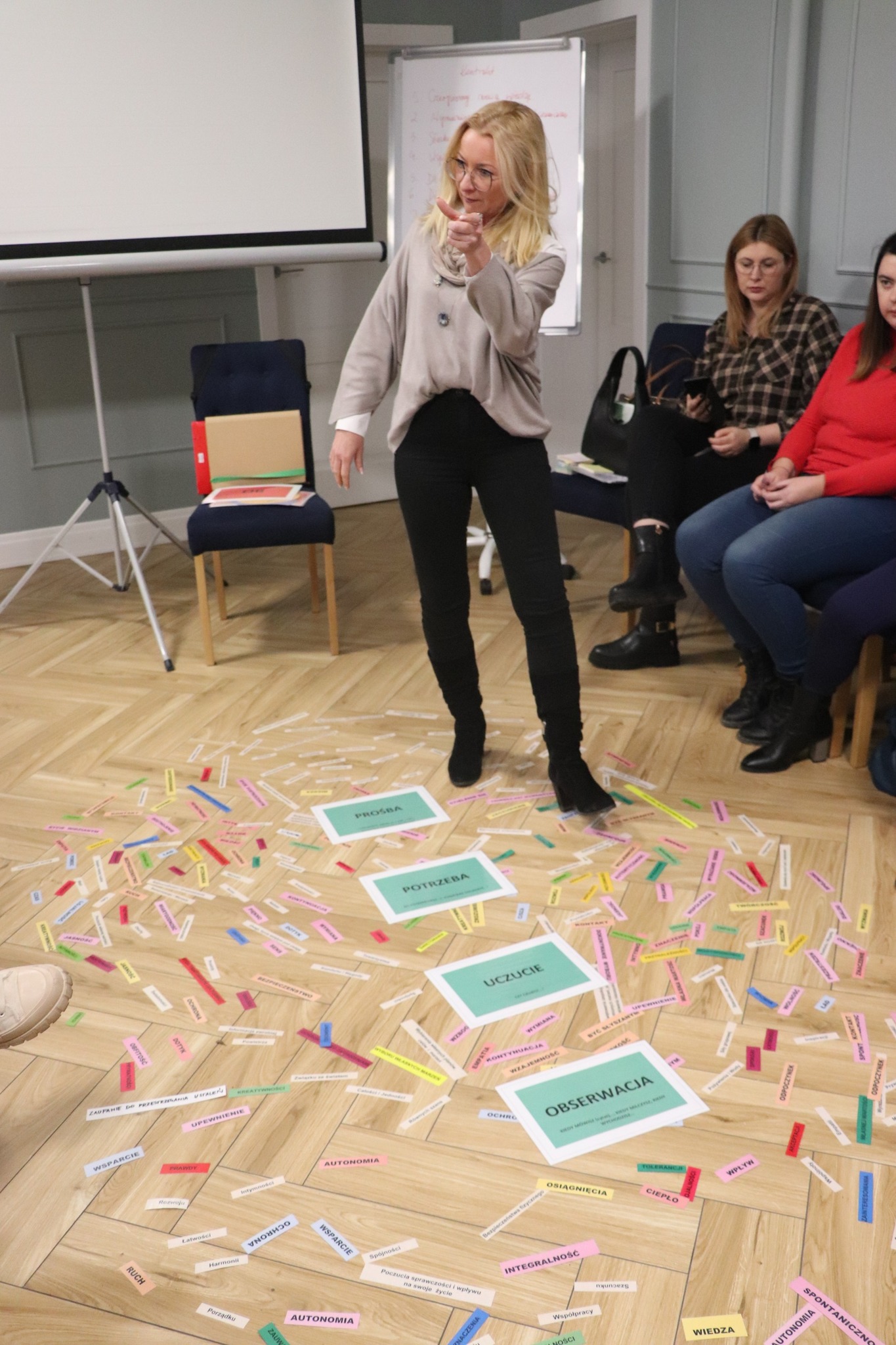 Kobieta stoi przed grupą ludzi, prowadząc dyskusję lub prezentację.