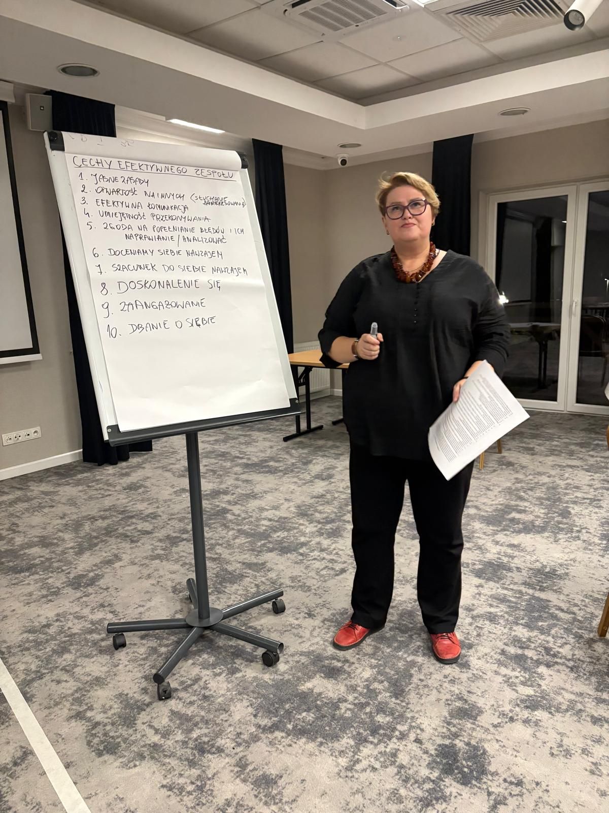Kobieta prezentuje treści na białej tablicy, stojąc w sali wykładowej