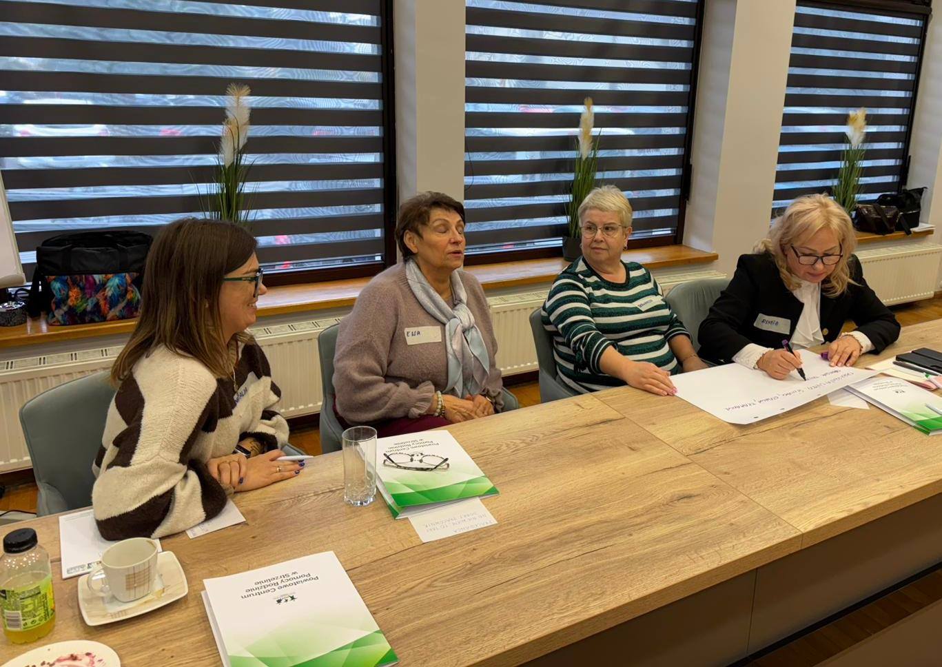 Grupa kobiet siedzi przy stole, przeglądając dokumenty i rozmawiając ze sobą.