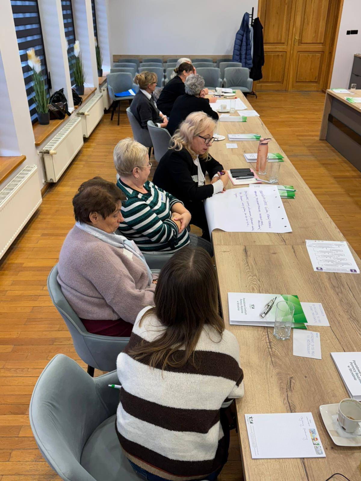 Grupa osób zgromadzona przy długim stole, prowadząca ożywioną dyskusję.