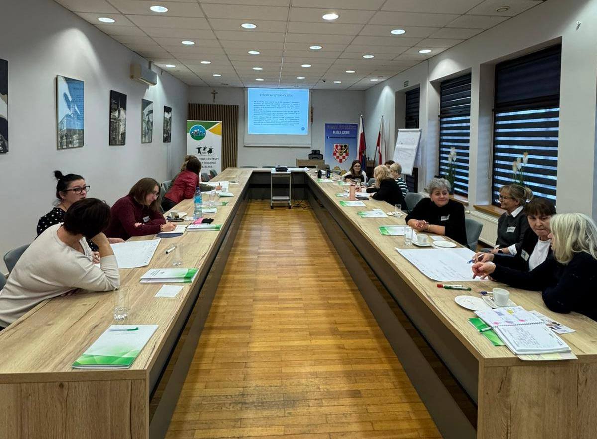 Osoby w sali konferencyjnej siedzą przy długich stołach podczas zebrania.