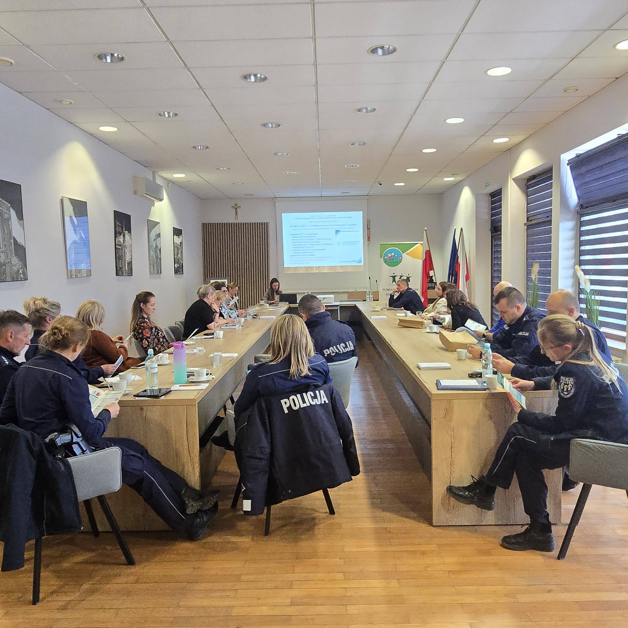 Duża grupa ludzi siedzi w sali wykładowej, zwrócona w stronę ekranu na którym wyświetlana jest prezentacja.