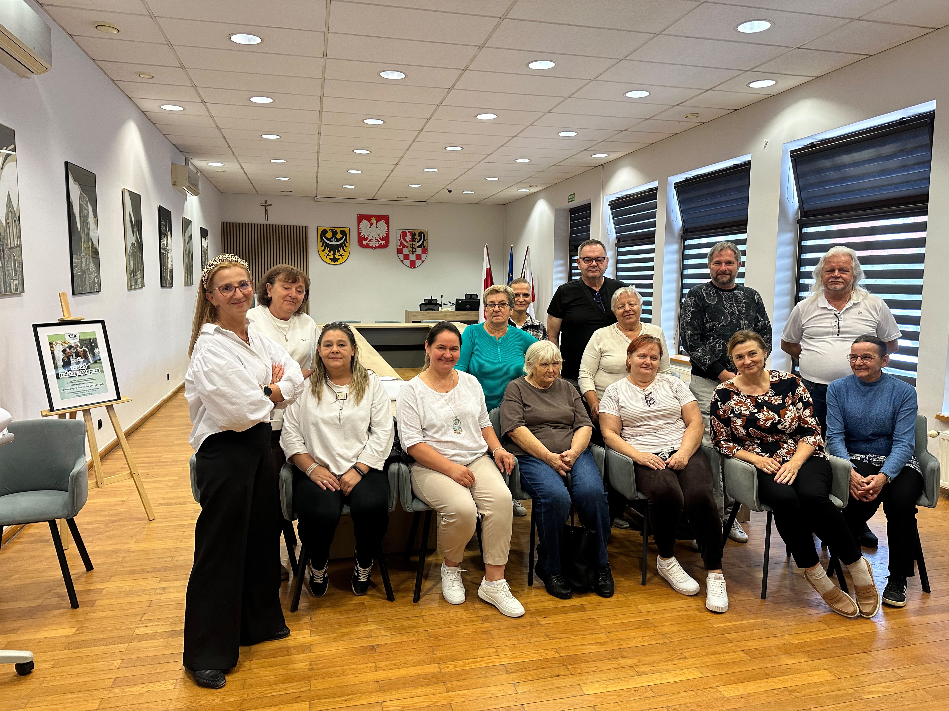 Grupa osób w pomieszczeniu, siedzących na krzesłach pozują do zdjęcia
