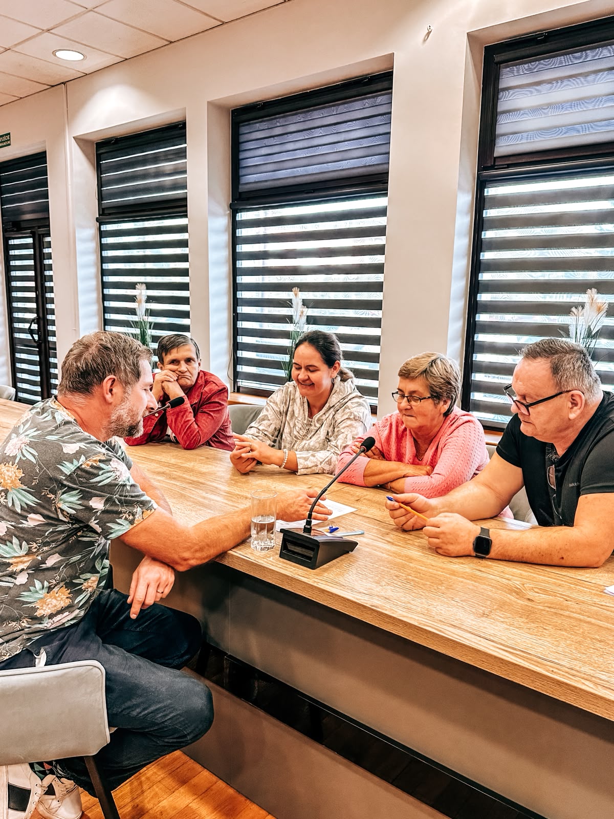Mężczyzna prowadzi rozmowę otoczony przez grupę osób przy stole.